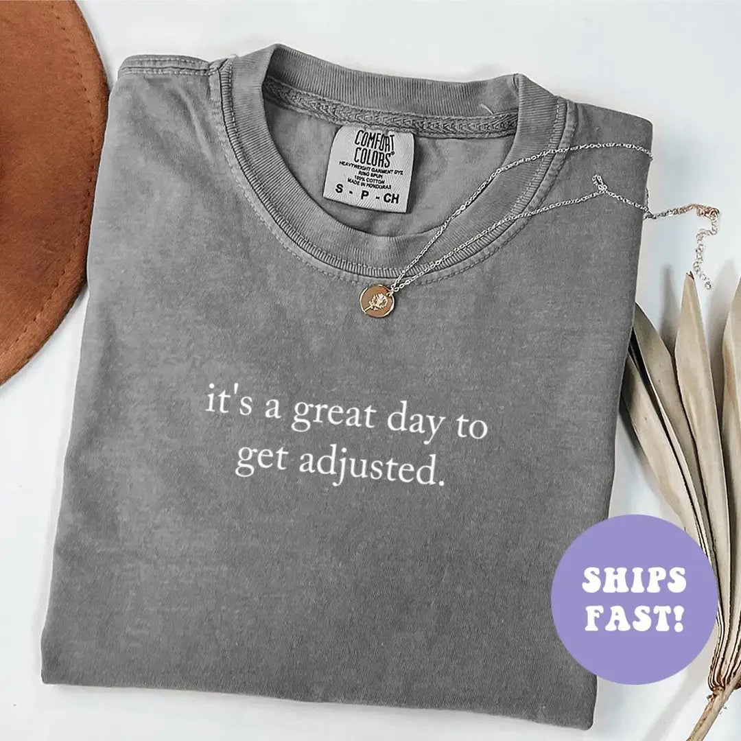 Folded Pepper Comfort Colors tee with it's a great day to get adjusted in white serif, necklace and brown hat