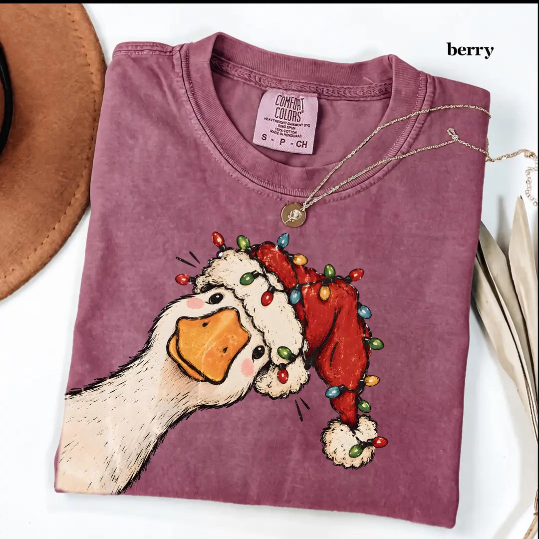 Folded Berry Comfort Colors tee in dusty magenta with a goose in a lit Santa hat, a brown hat and leaves at the edges