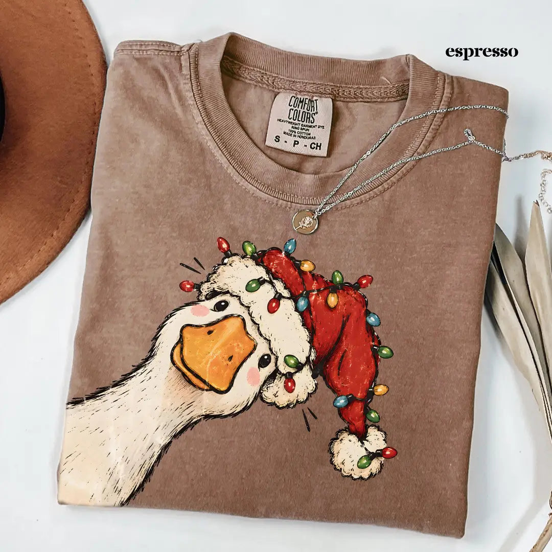 Folded Espresso brown Comfort Colors tee with the Santa hat goose wrapped in string lights, styled with a necklace