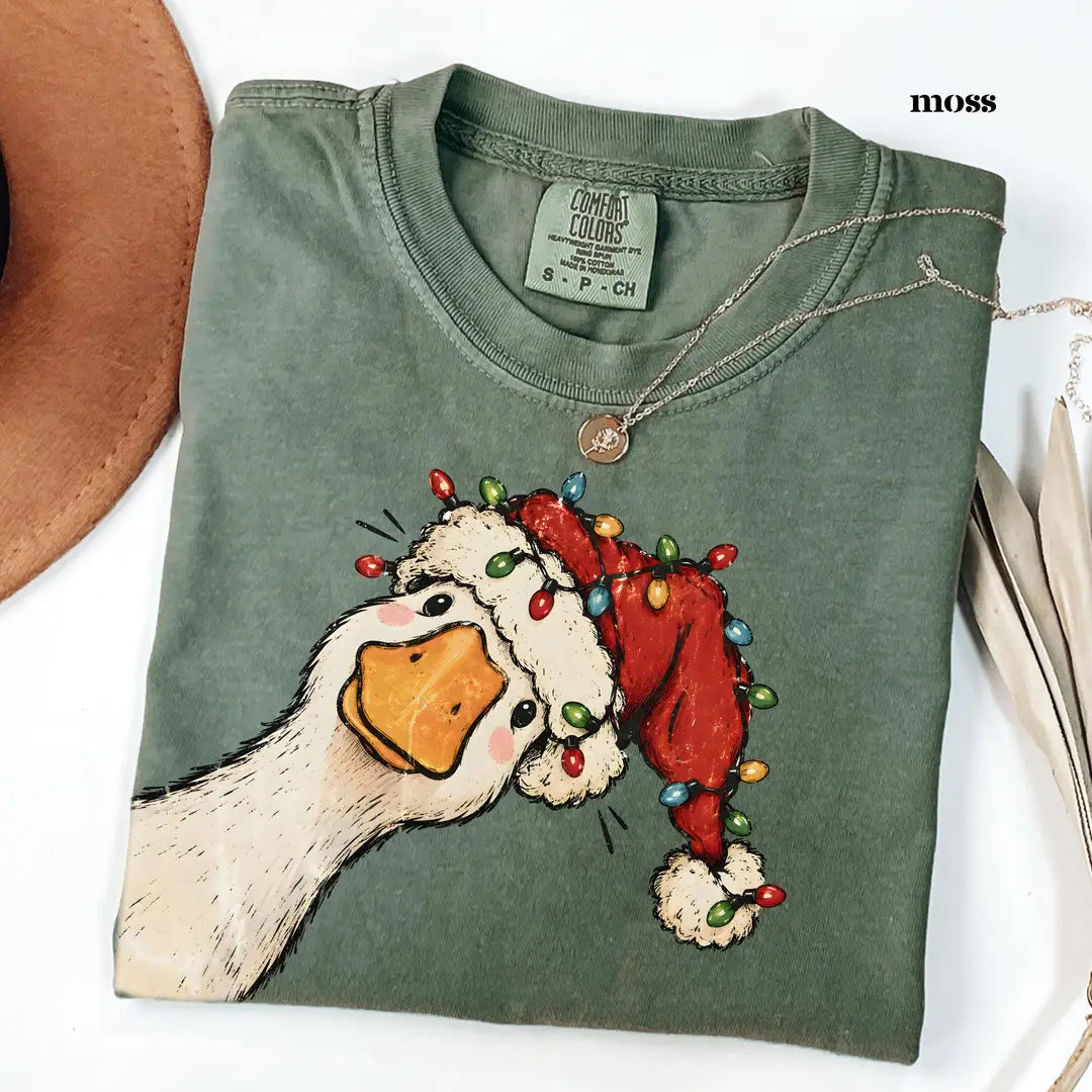 Folded Moss green Comfort Colors tee with the goose in a Santa hat and multicolor string lights, neck label visible