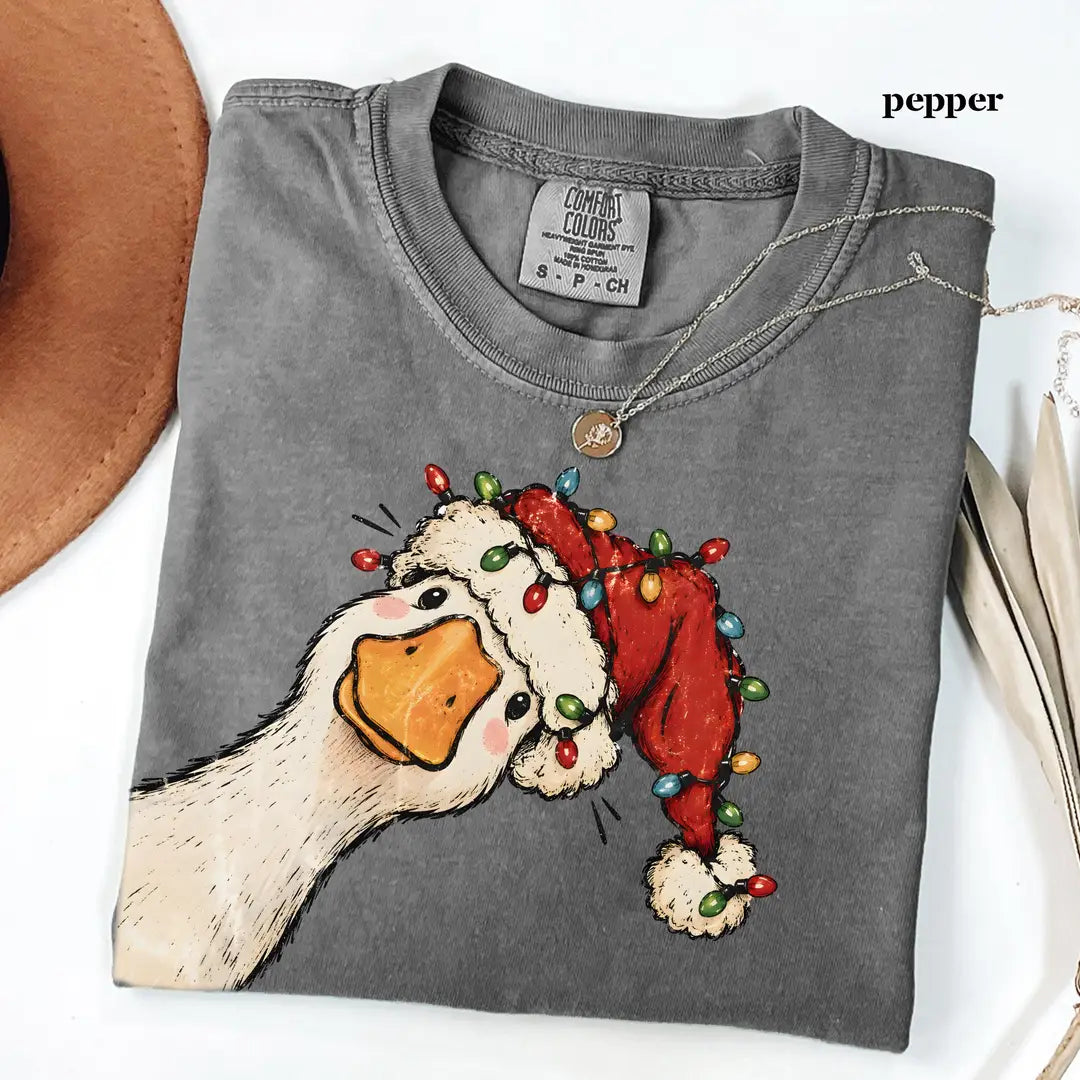 Folded Pepper Comfort Colors tee with a goose peeking out in a red Santa hat wrapped in colorful string lights