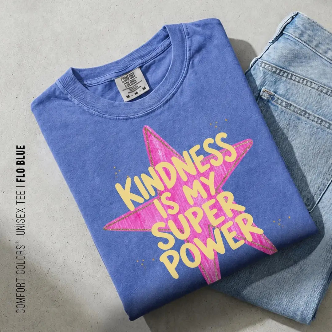 Folded Flo Blue Comfort Colors tee on blue jeans with yellow kindness lettering and a large pink star