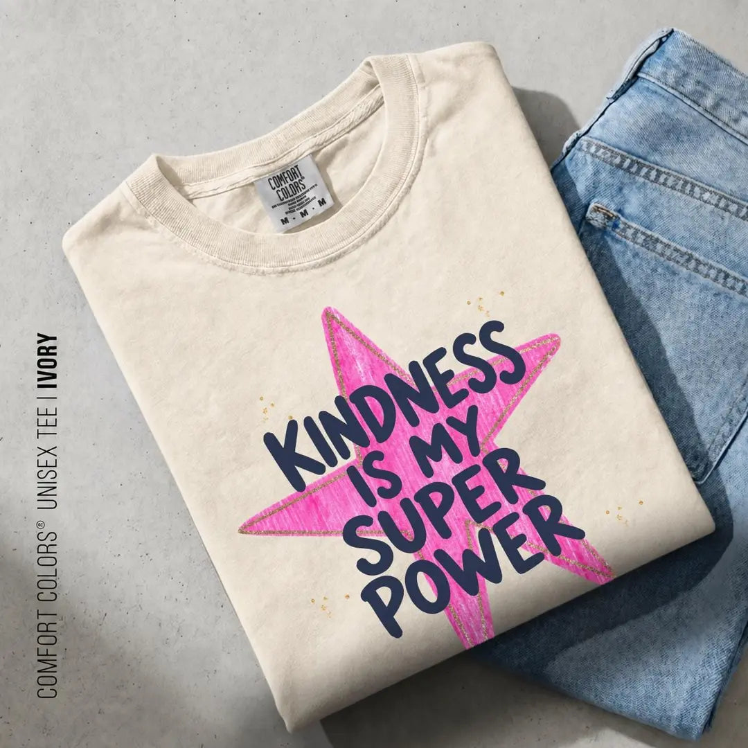 Folded Ivory Comfort Colors tee on blue jeans with navy kindness is my super power lettering over a pink star