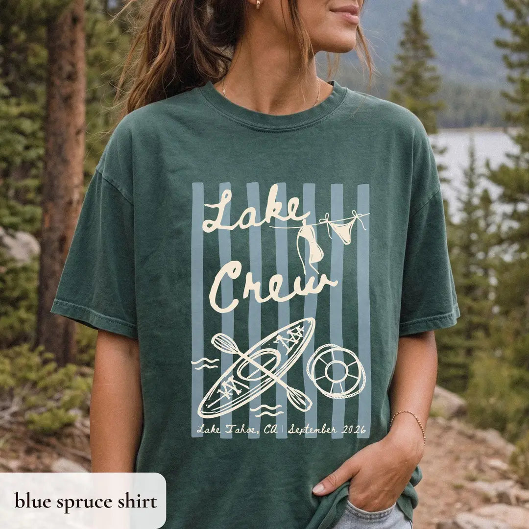 Woman in a Blue Spruce Comfort Colors tee among tall pines, ivory lake crew script over stripes with kayak and life ring