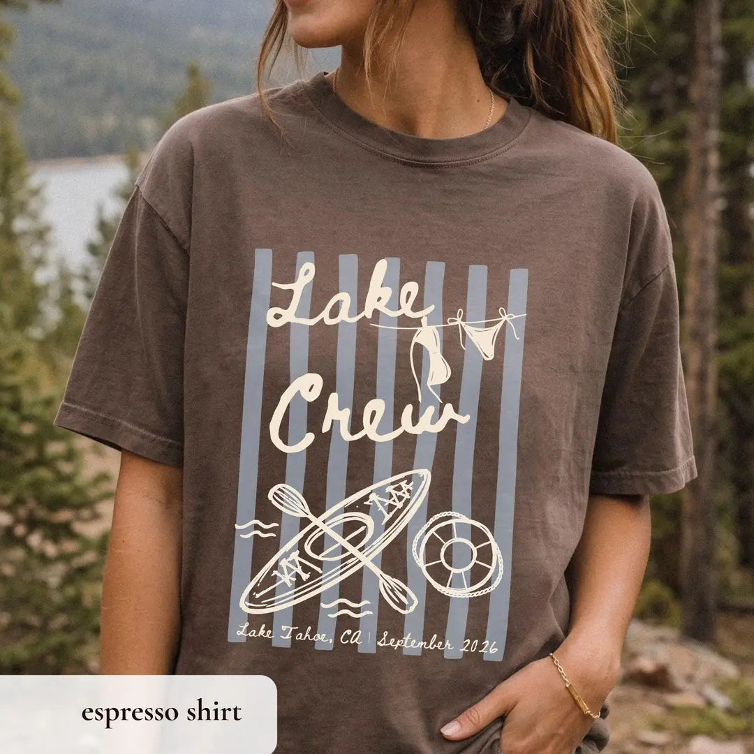 Woman in an Espresso brown Comfort Colors tee on a lake trail, ivory lake crew over gray stripes with kayak and life ring