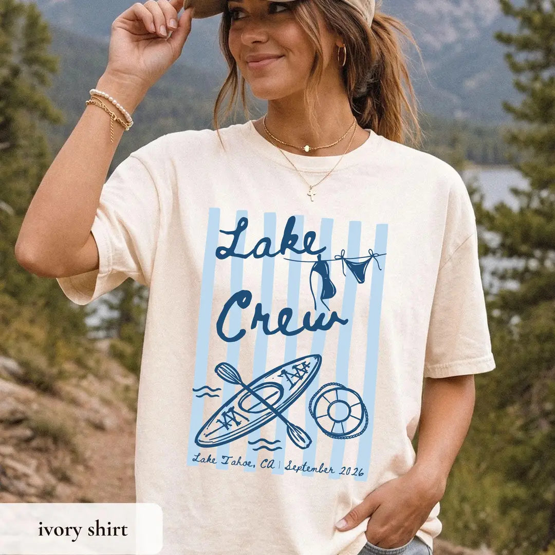 Woman in an Ivory Comfort Colors tee, hand on her hat, blue lake crew lettering on light blue stripes with a kayak