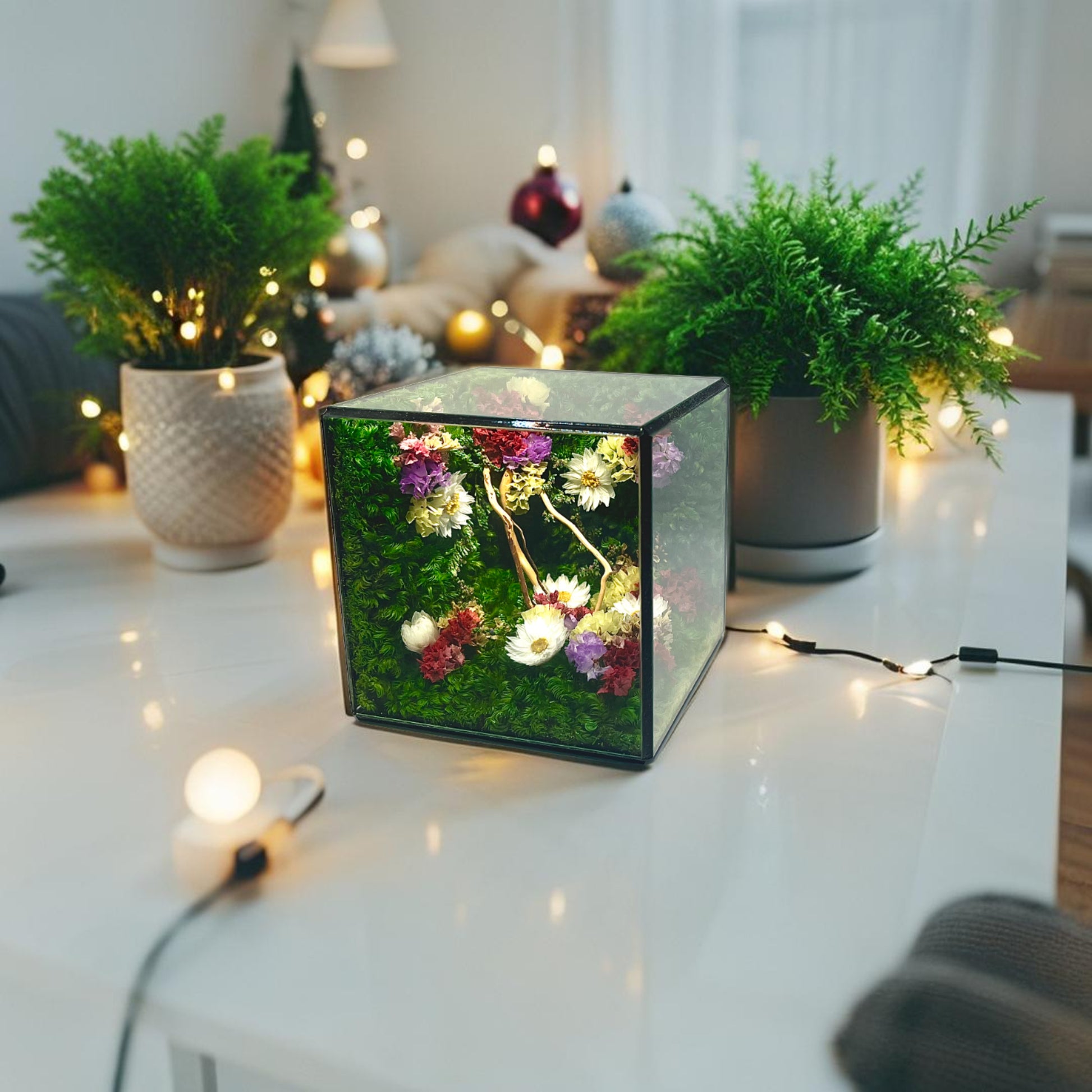 Decorative LED light cube on a table with plants and string lights in the background
