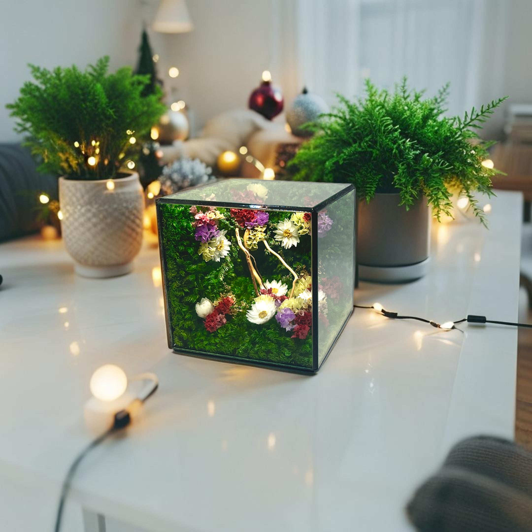 Decorative LED light cube on a table with plants and string lights in the background