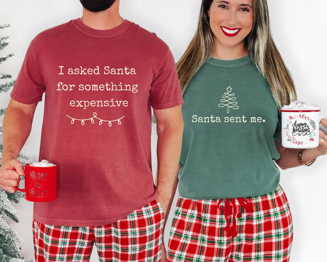 Christmas couple wearing Crimson 'I asked Santa for something expensive' and Blue Spruce 'Santa sent me' Comfort Colors T-shirts.