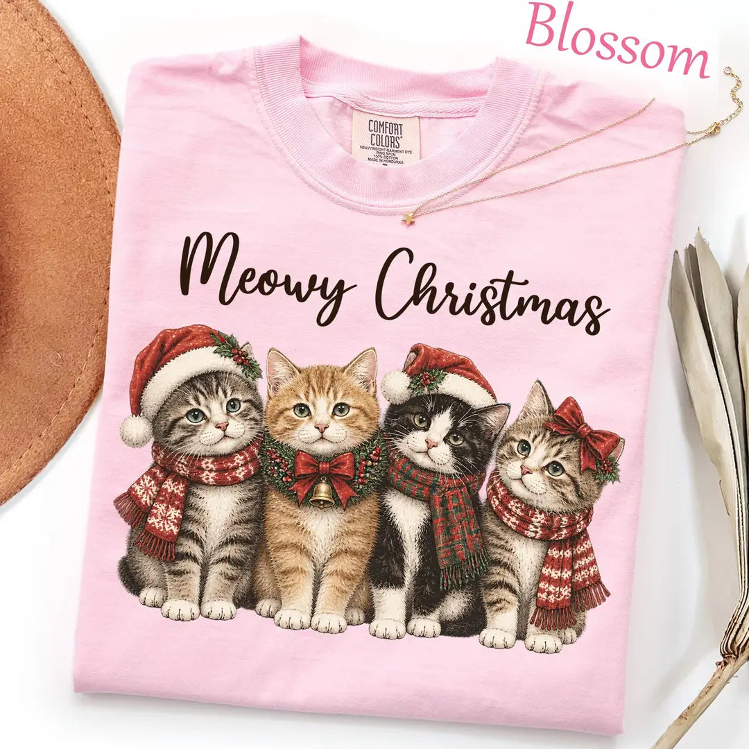 Folded Blossom pink Comfort Colors tee with black meowy christmas script and four kittens in santa hats and red scarves