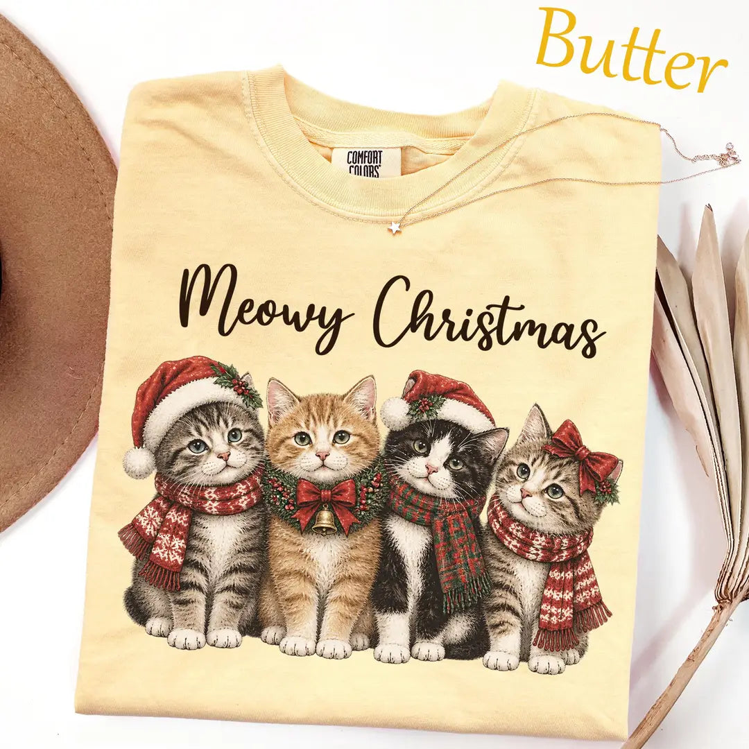 Folded Butter yellow Comfort Colors tee with black script meowy christmas above four kittens in santa hats and plaid scarves