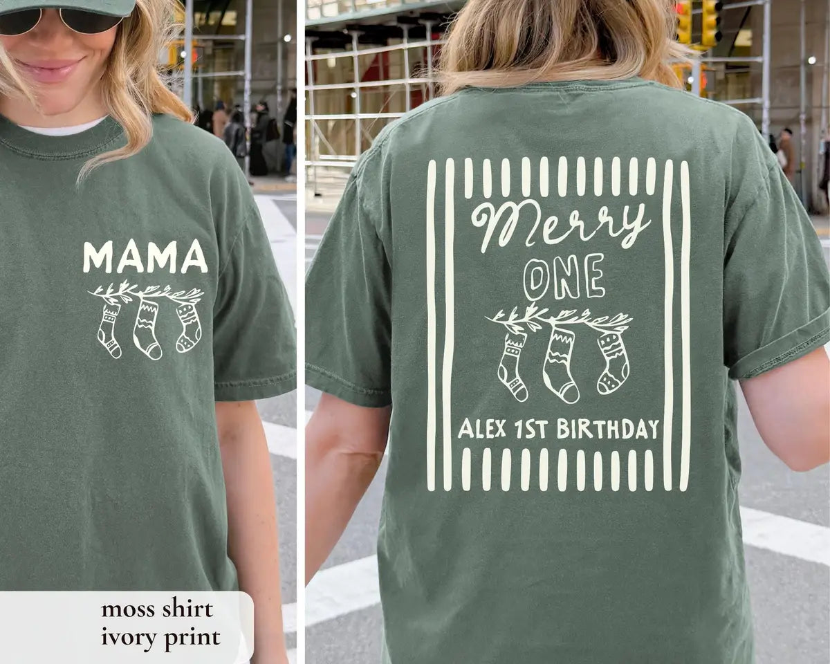 Woman in a Moss green Comfort Colors tee, front with an ivory MAMA stocking print and back with Merry ONE Alex 1st Birthday
