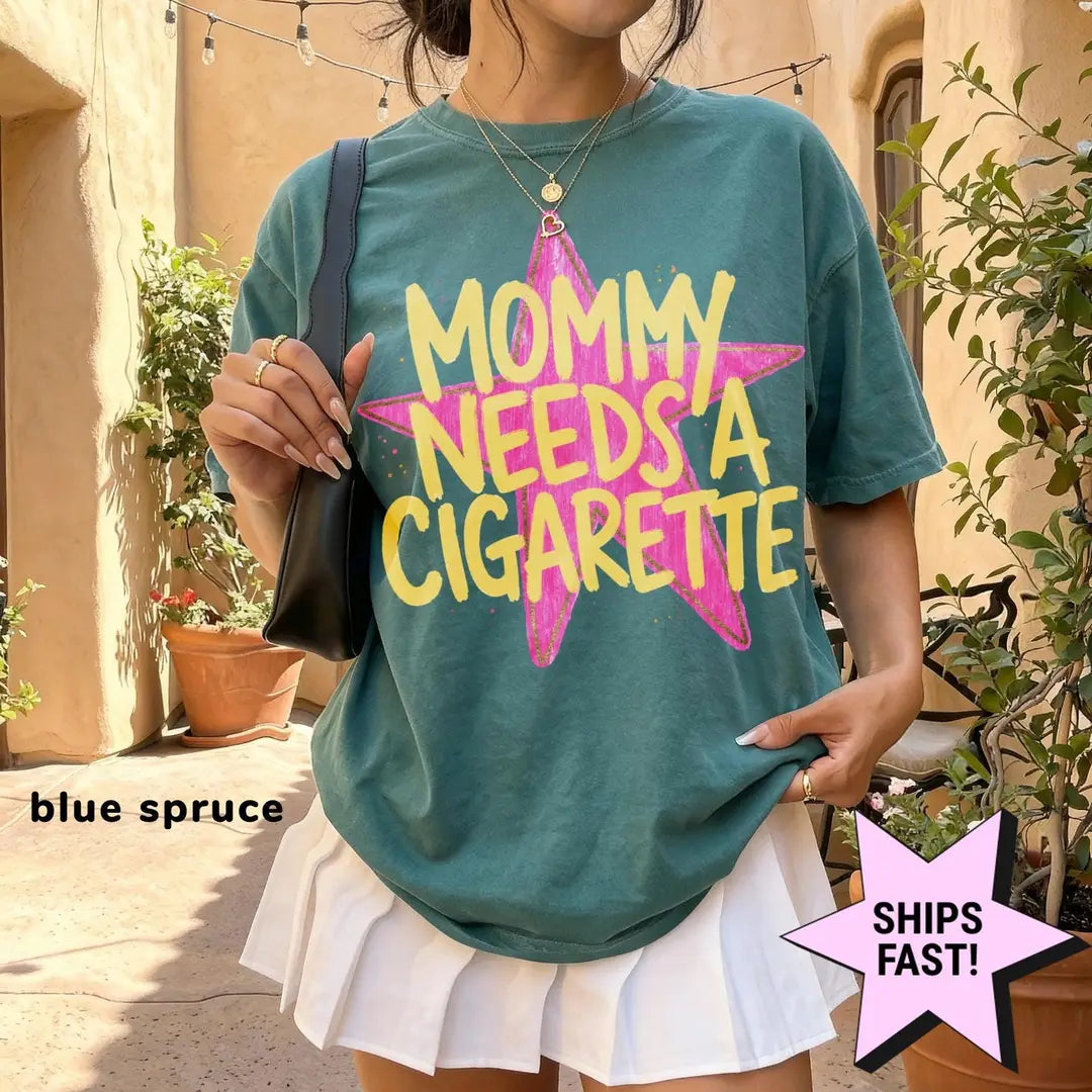 Woman in a Blue Spruce Comfort Colors tee and a white skirt in a courtyard, yellow mommy needs a cigarette on pink