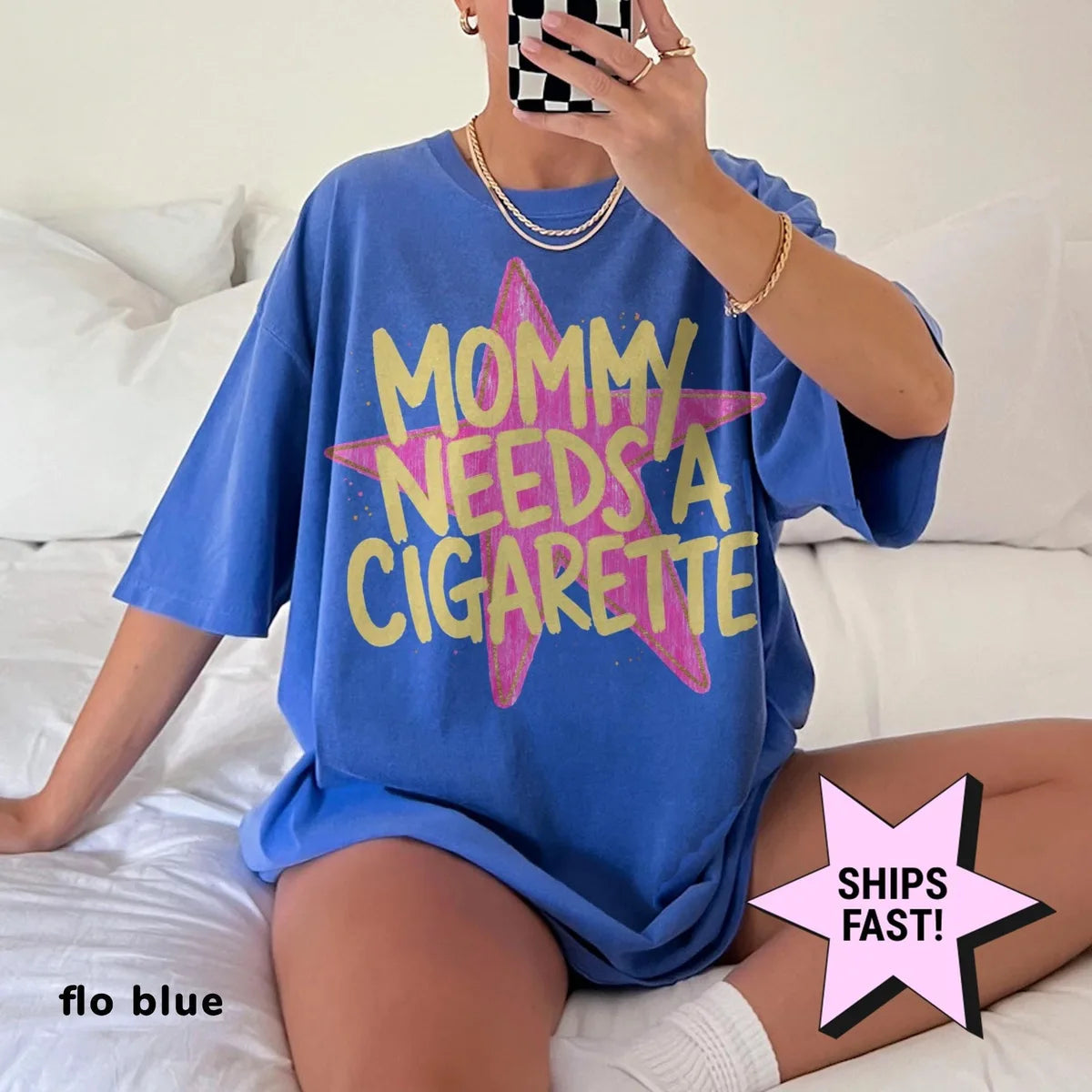 Woman in a Flo Blue Comfort Colors tee taking a mirror selfie on a bed, yellow mommy needs a cigarette on a pink star