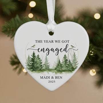 Heart-shaped ornament with a forest design and text 'The Year We Got Engaged' on a Christmas tree.