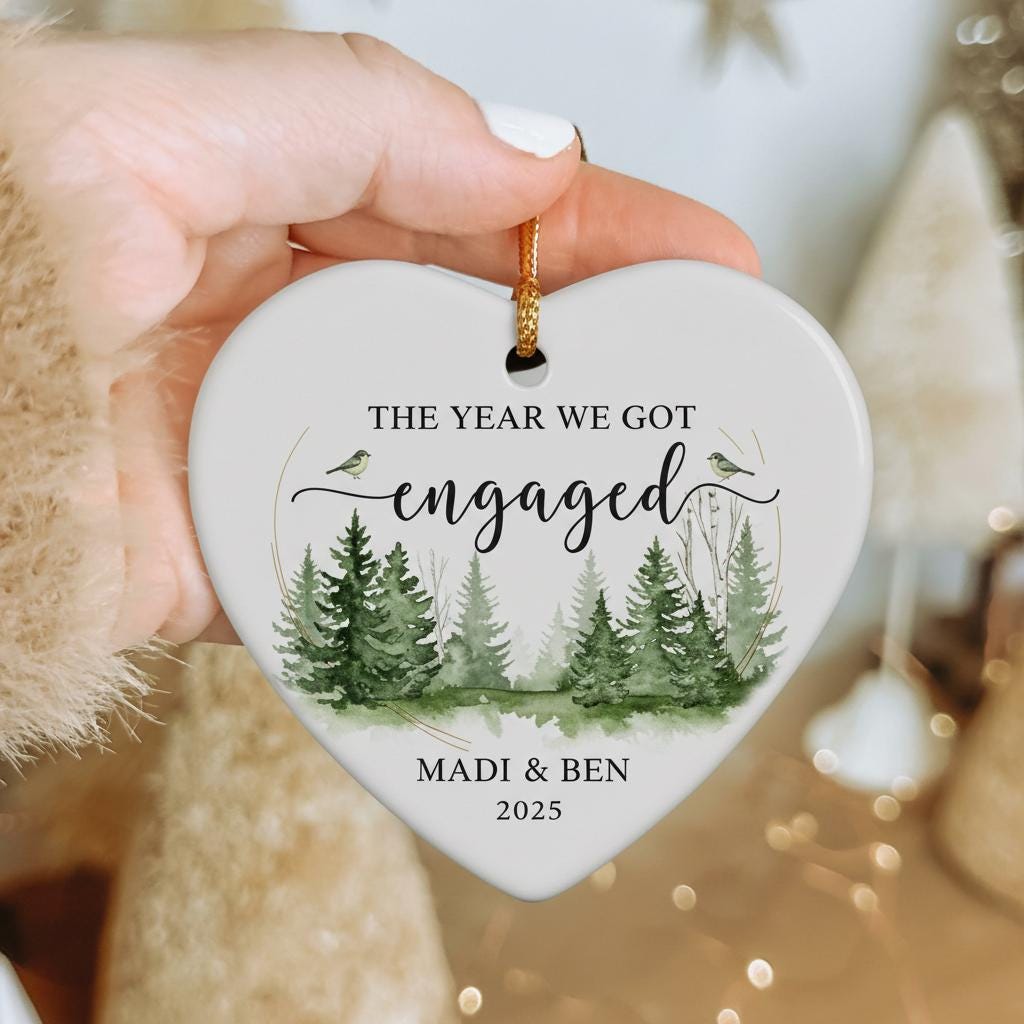 Heart-shaped ornament with a forest design and text 'The Year We Got Engaged' on a Christmas tree.
