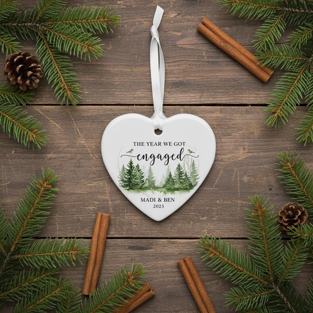 Heart-shaped ornament with 'The Year We Got Engaged' text on a wooden surface with pine branches and cinnamon sticks.