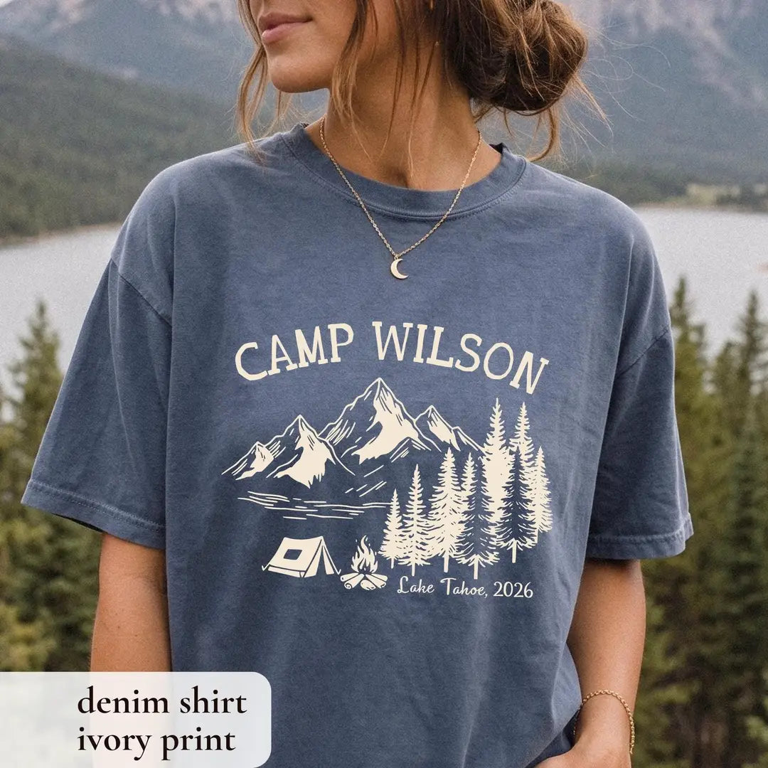 Woman in a Denim Comfort Colors tee wearing a crescent moon necklace, ivory Camp Wilson over a lake, pines, tent and campfire
