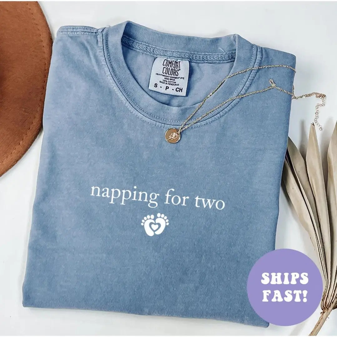 Folded Blue Jean Comfort Colors tee with napping for two in white serif and a small baby feet heart, necklace on the collar