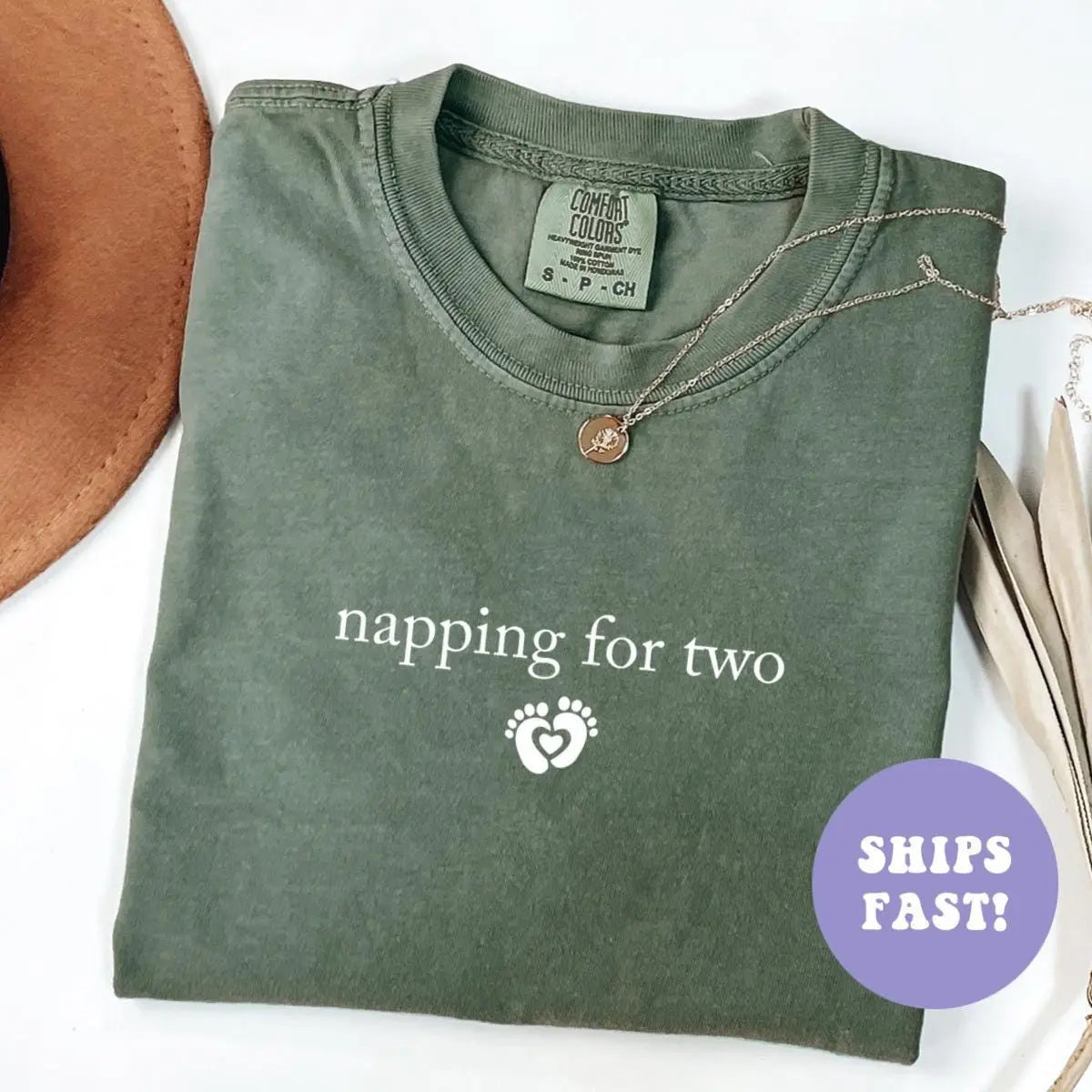 Folded Moss green Comfort Colors tee with napping for two above a white baby feet heart icon, necklace on the collar