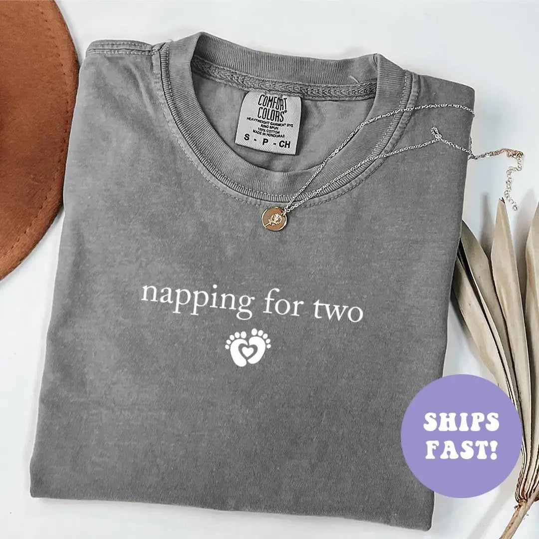 Folded Pepper Comfort Colors tee with napping for two in white serif above baby feet in a heart, brown hat beside it