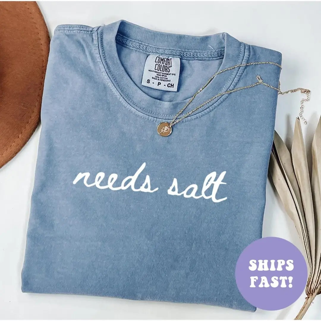 Folded Blue Jean Comfort Colors tee with the words needs salt in white cursive across the chest