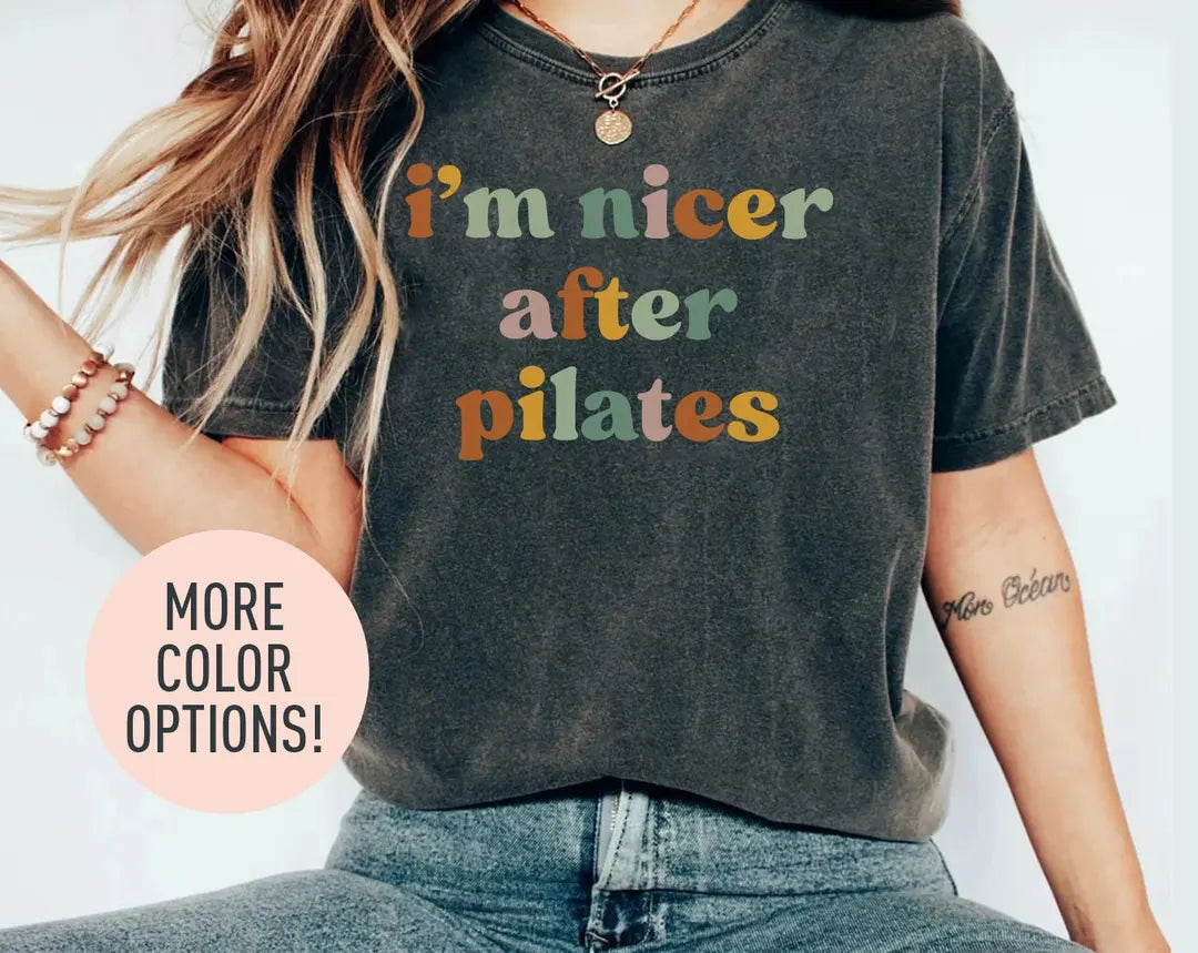 Woman in a dark gray Comfort Colors tee and jeans, bracelets, with i'm nicer after pilates in green, rose and rust letters