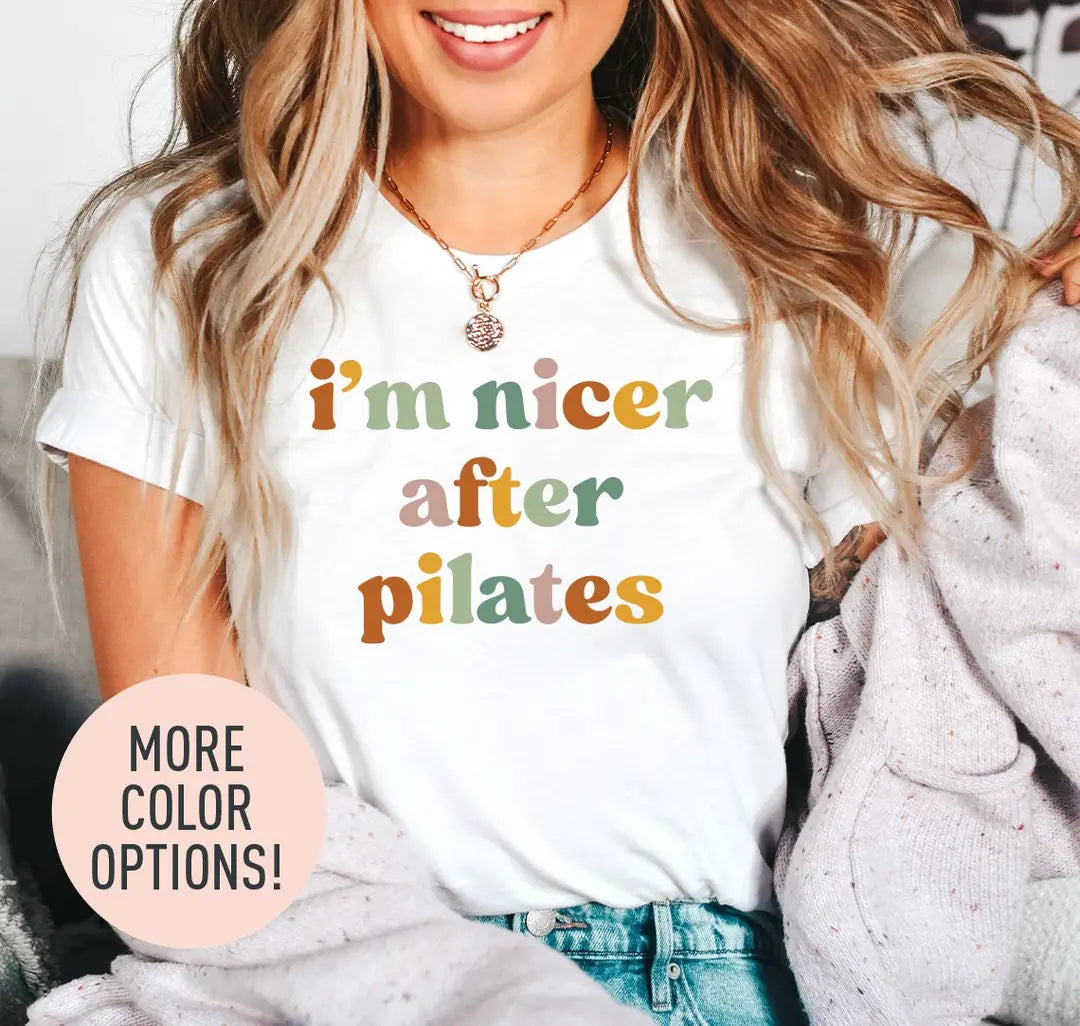 Woman in a white tee and a lilac cardigan, i'm nicer after pilates stacked in rust, sage and rose retro lettering