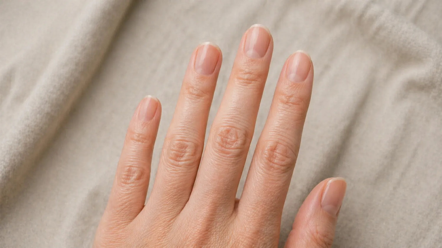 Close-up of a hand with natural nail polish on a beige fabric background