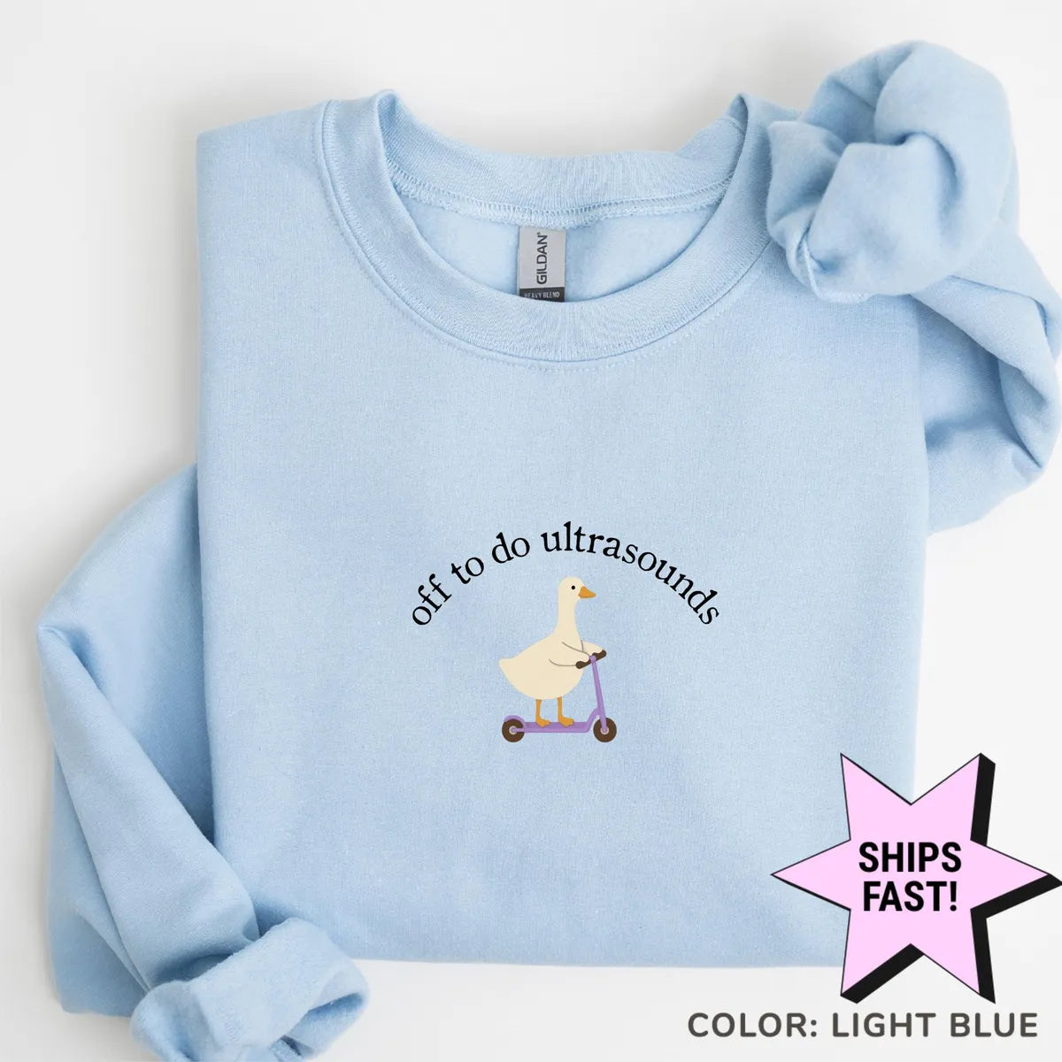 Light Blue crewneck sweatshirt laid flat, a goose on a purple scooter beneath arched black text, off to do ultrasounds