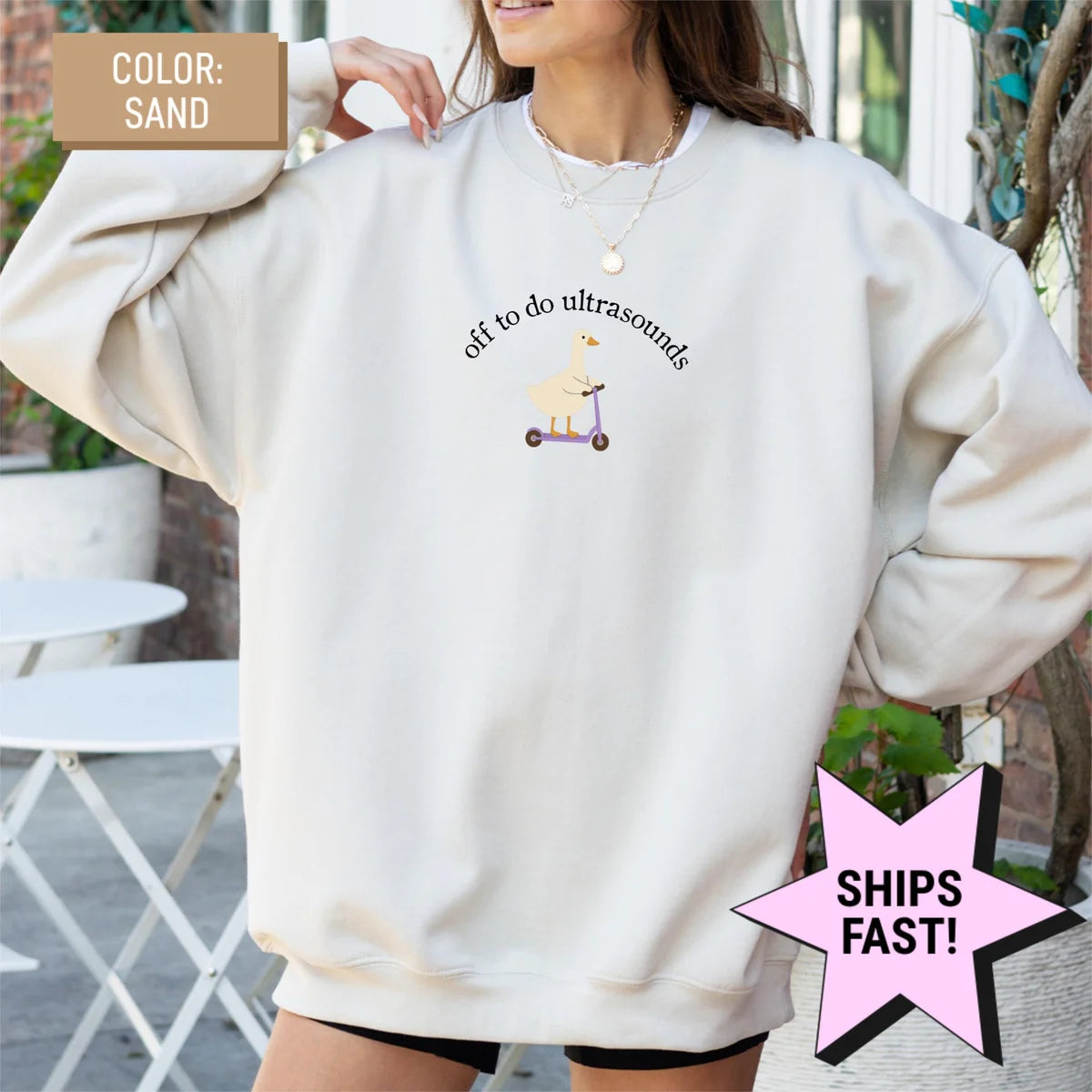 Woman in an oversized Sand crewneck sweatshirt, hands at her shoulders, goose on a purple scooter with arched ultrasound text