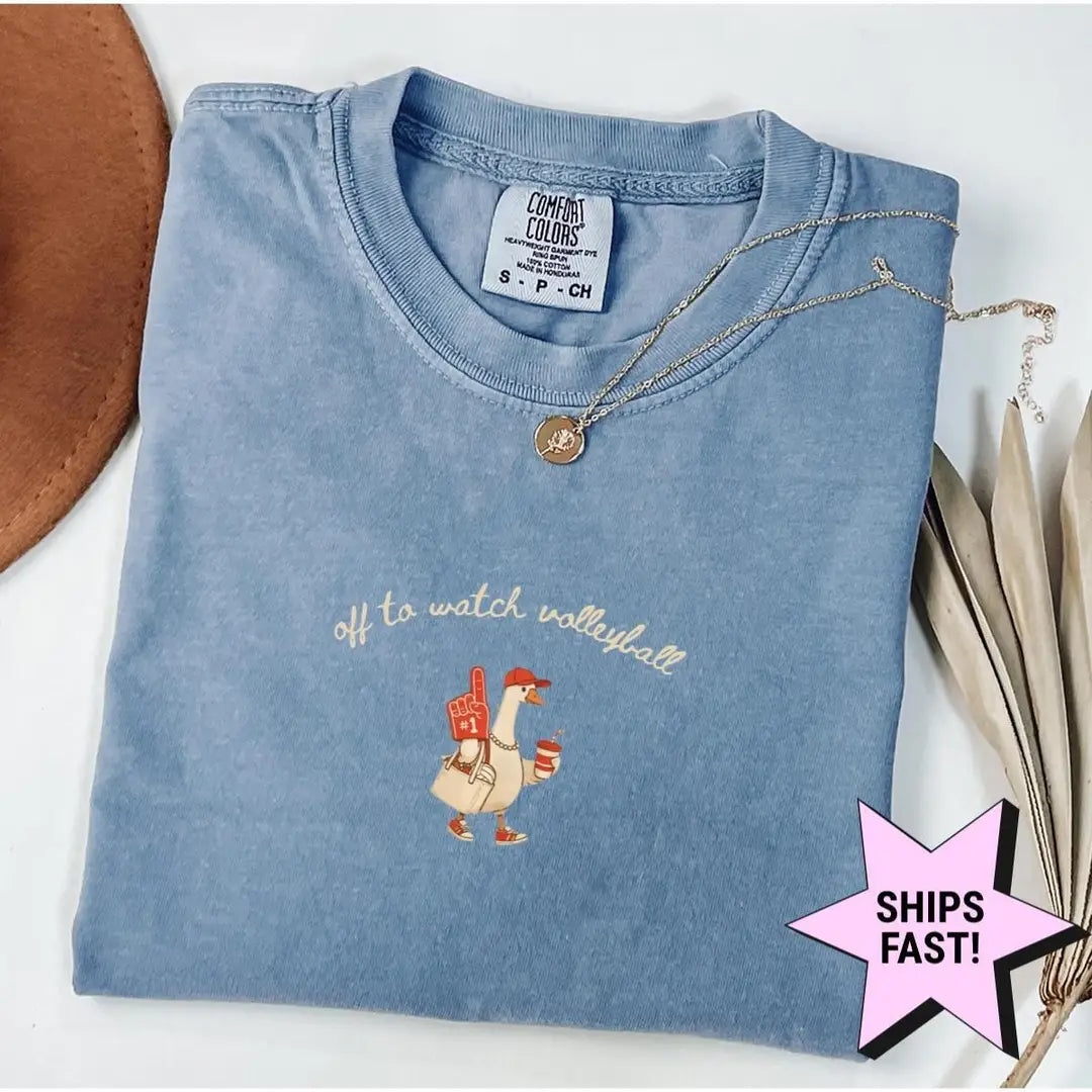 Folded Blue Jean Comfort Colors tee with the goose and Off to Watch Volleyball print, styled with a gold necklace