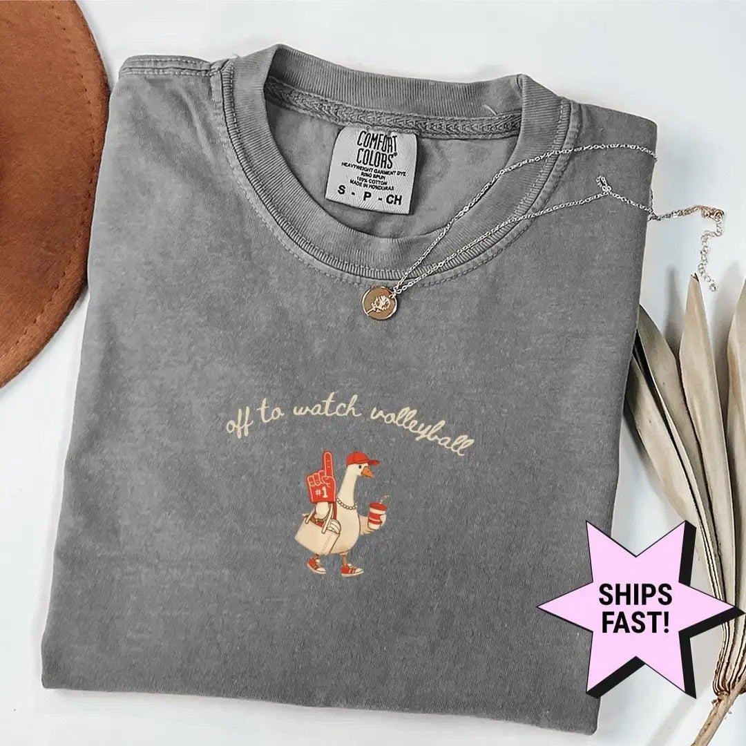 Folded Pepper Comfort Colors T-shirt with a goose holding a foam finger and a drink under Off to Watch Volleyball in cursive