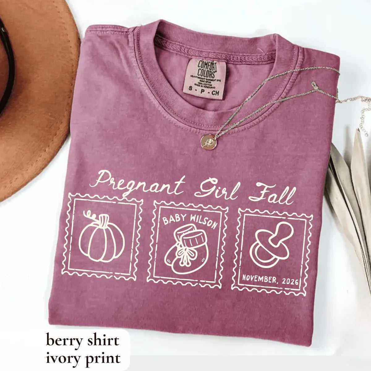 Folded Berry Comfort Colors tee with ivory pregnant girl fall script, a pumpkin stamp, a baby bootie and a pacifier
