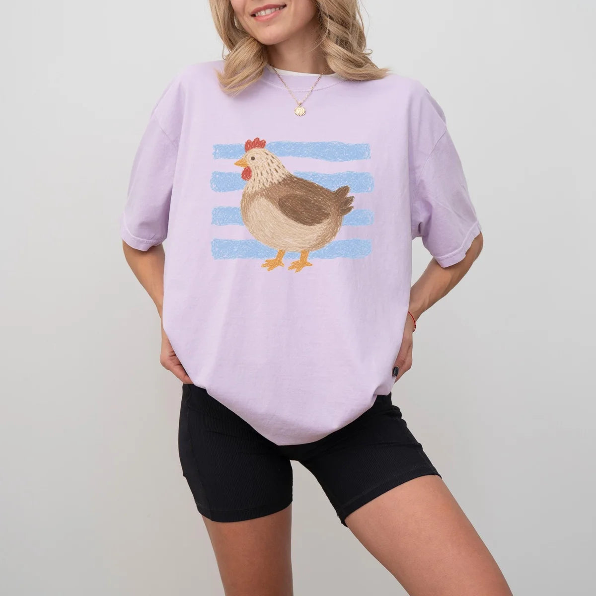 Woman in an Orchid lavender Comfort Colors tee and black shorts, brown hen on light blue stripes
