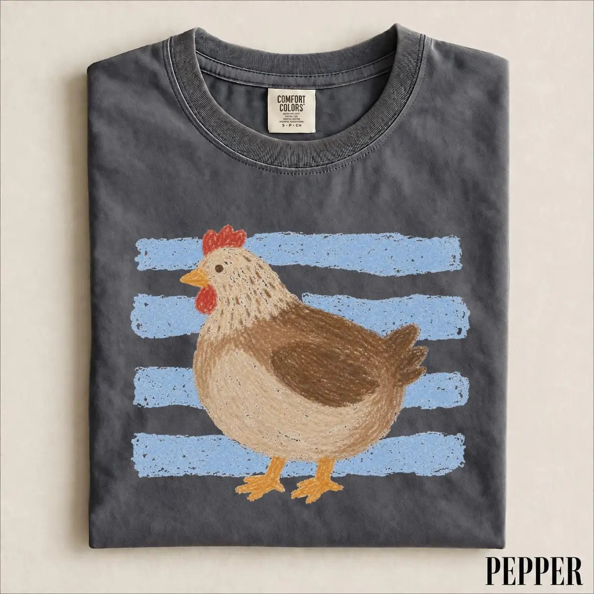 Folded Pepper Comfort Colors tee with a hand-drawn brown hen standing in front of light blue brush stripes