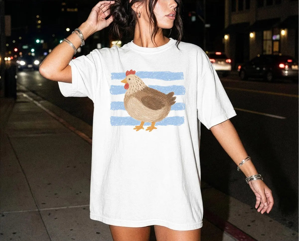 Woman in a White Comfort Colors tee on a night street, a brown hen and light blue brush stripes on the chest