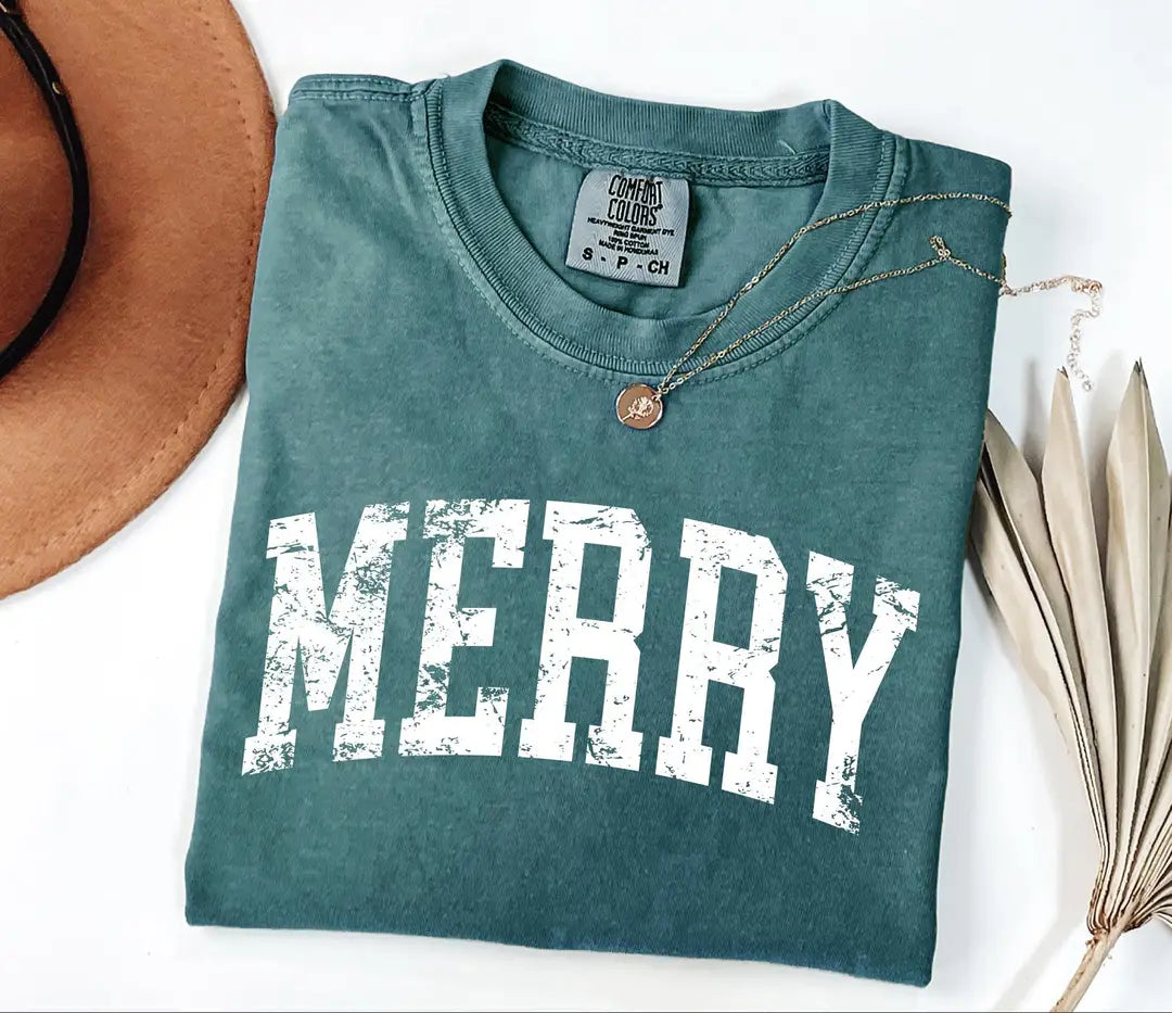 Blue Spruce Comfort Colors T-shirt with bold white 'MERRY' holiday lettering, folded mockup.
