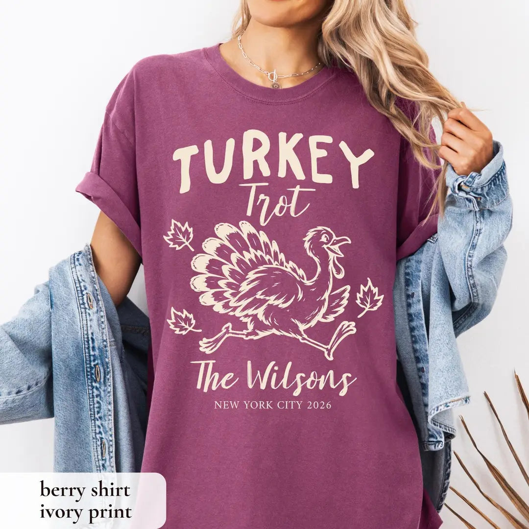 Woman in a Berry Comfort Colors tee and a denim jacket, cream Turkey Trot lettering above a running turkey and leaves