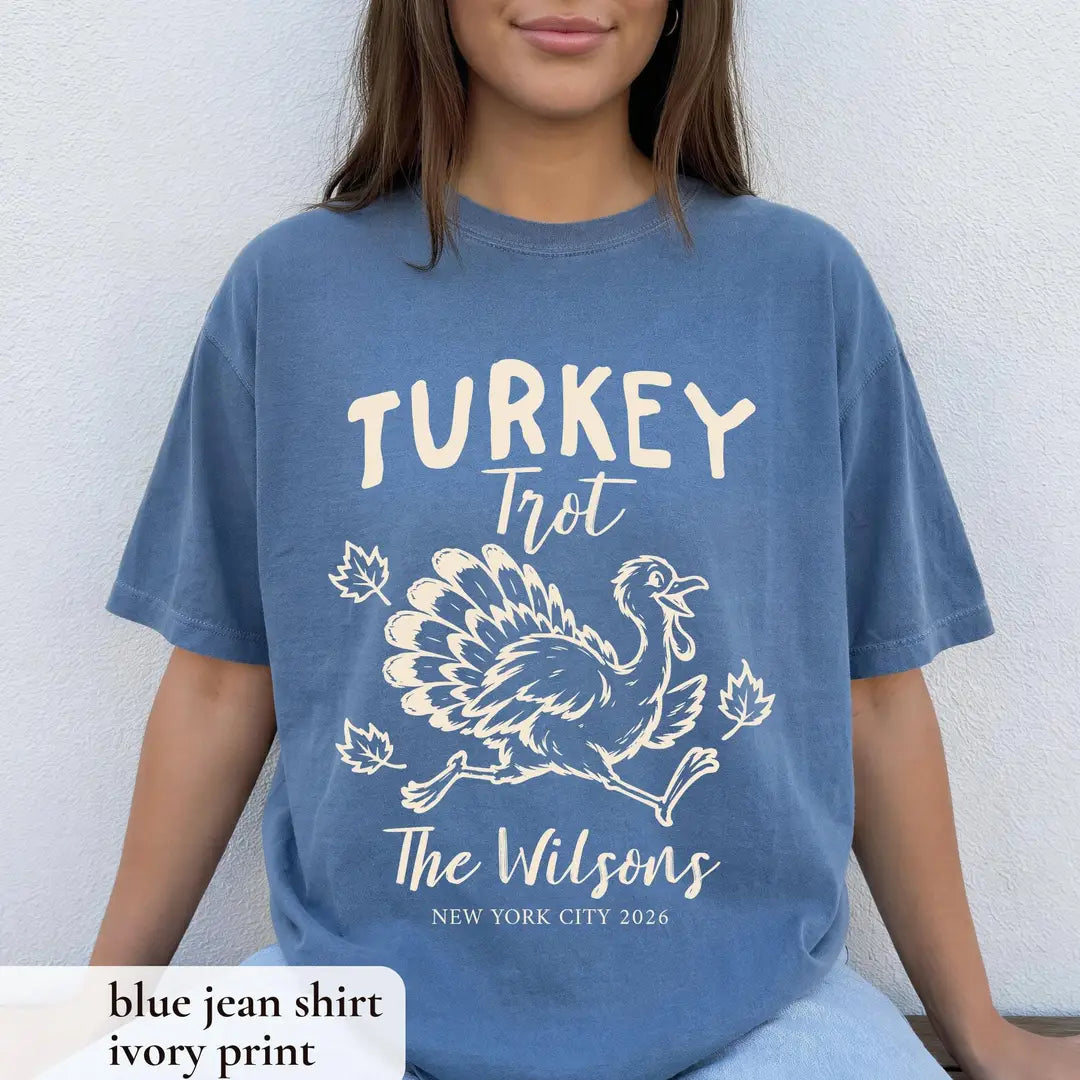 Woman in a Blue Jean Comfort Colors tee seated against a white wall, cream Turkey Trot turkey and The Wilsons