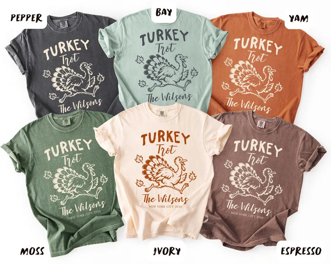 Six folded Comfort Colors tees in Pepper, Bay, Yam, Moss, Ivory and Espresso, each with a Turkey Trot running turkey design