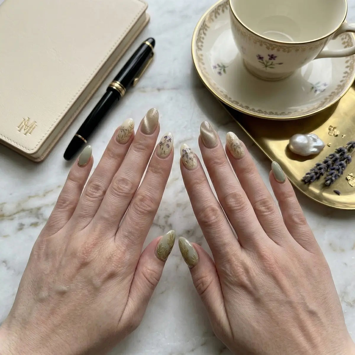 Close-up of hands with decorative nail art on a marble surface with a tea cup and saucer.