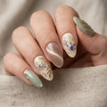 Close-up of a hand with decorative nails featuring floral and leaf designs.