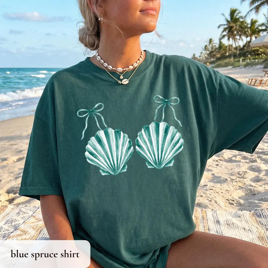 Woman in a Blue Spruce Comfort Colors tee on the sand, teal striped scallop shells tied with tiny bows