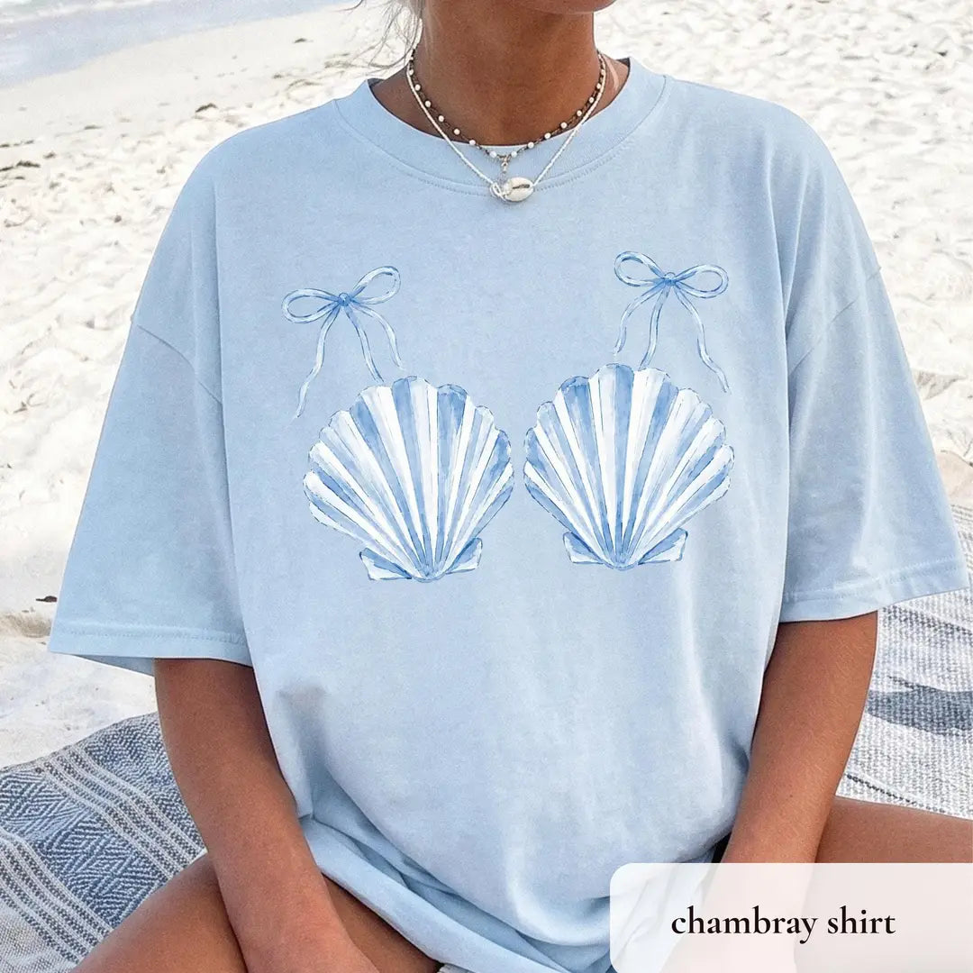 Woman in a Chambray blue Comfort Colors tee on a beach blanket, two blue striped scallop shells tied with bows