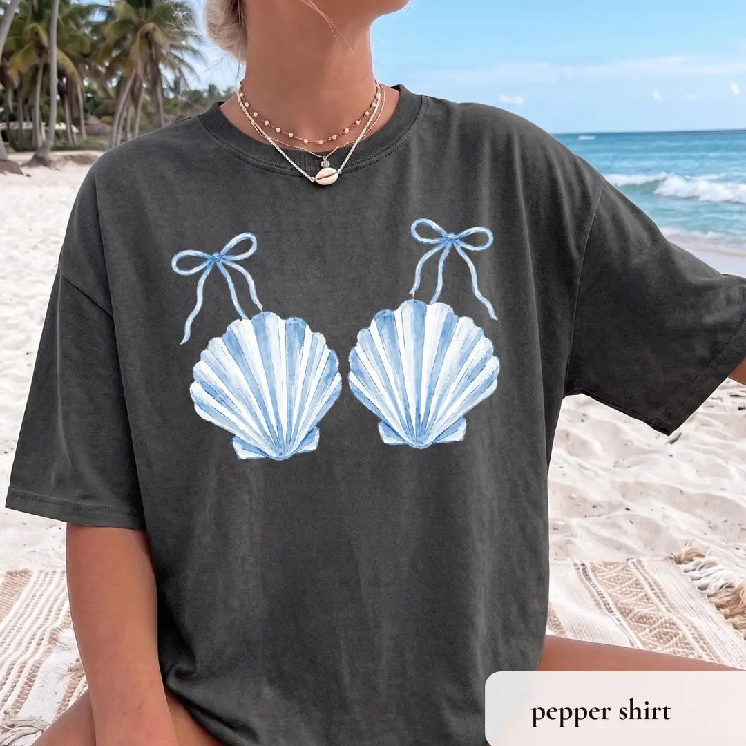 Woman in a Pepper Comfort Colors tee on a sunny beach with two blue striped scallop shells tied with tiny bows