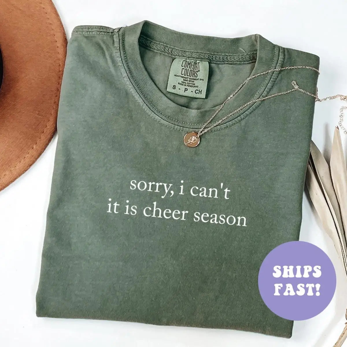 Folded Moss green Comfort Colors tee with sorry, i can't it is cheer season in white serif type