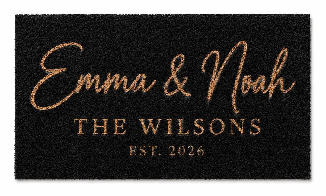 Flat view of a black faux coir doormat with two script first names, a family name line, and an established year