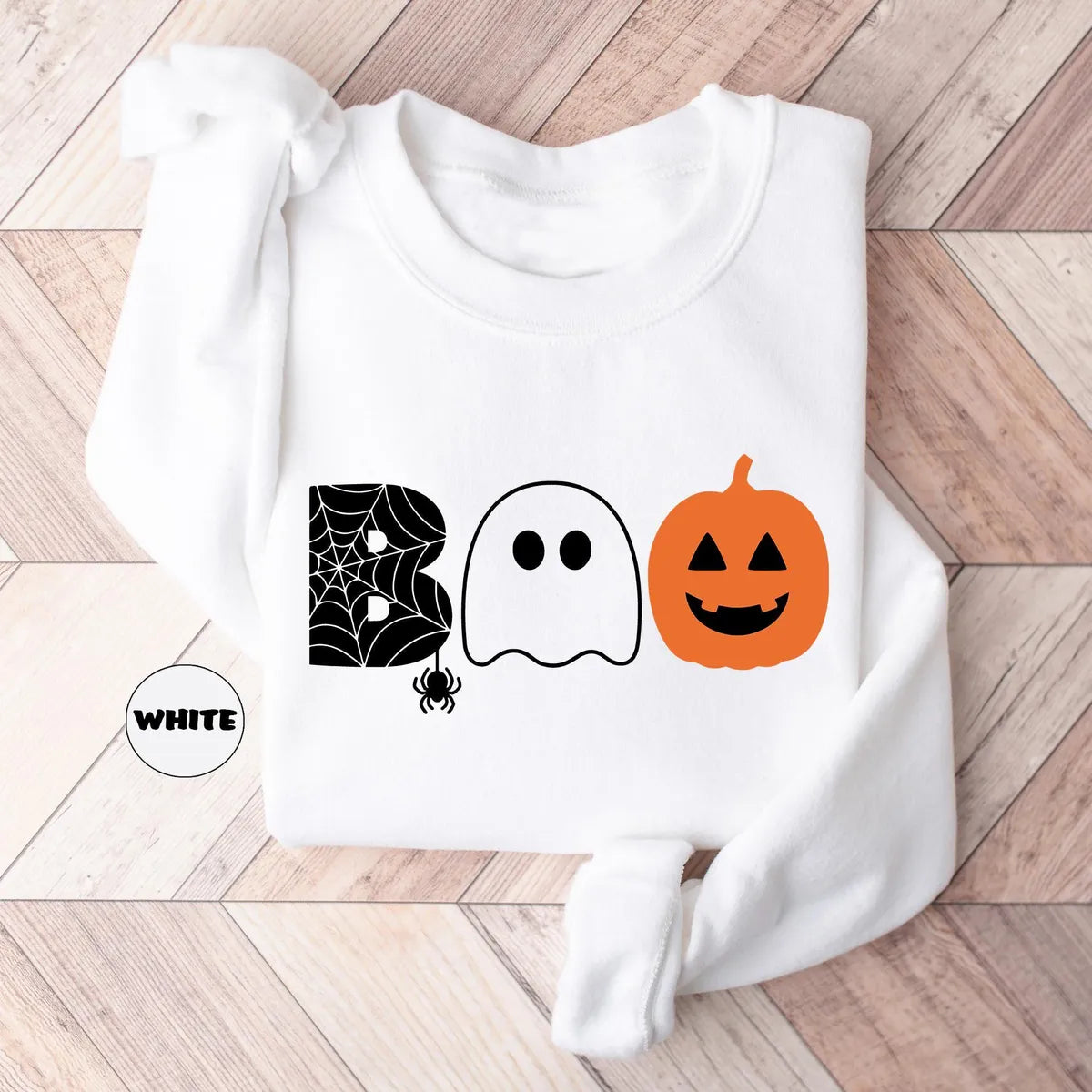 White crewneck sweatshirt with the word boo spelled with a spider web letter, a ghost and a jack-o-lantern, flat lay view.