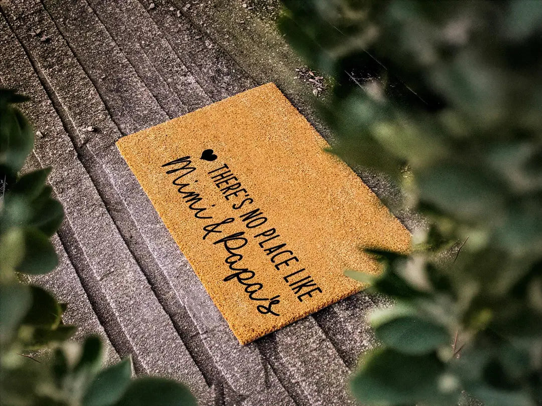Coir doormat with a There's No Place Like Mimi and Papa's message on weathered gray planks with leafy branches